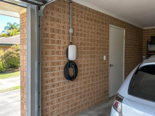Wall-mounted EV charger with coiled cable on a brick garage wall beside a parked car in Arundel